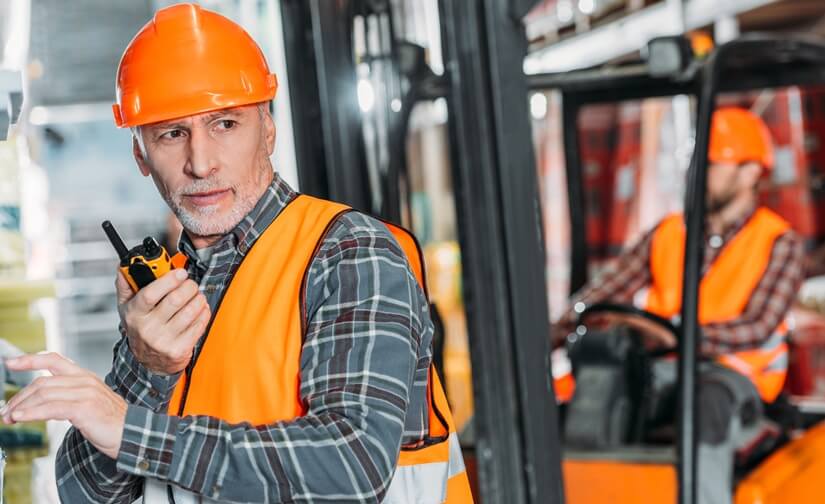 warehouse worker with orange hardhat, using a walkie talkie