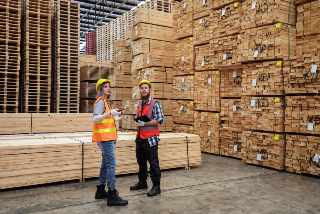 Builders merchant staff using a two way radio while checking timber stock in a busy timber yard warehouse.